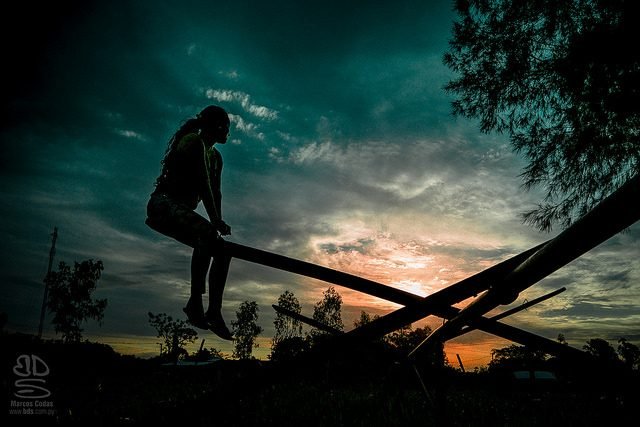 Una figura sentada en un subibaja, en silueta contra el cielo del atardecer.