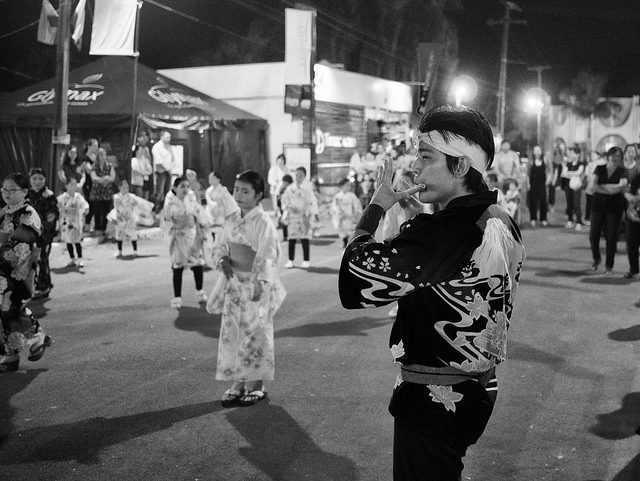 Blanco y negro: un festival callejero de noche, con bailarines en yukata detrás de un hombre con una chaqueta estampada.